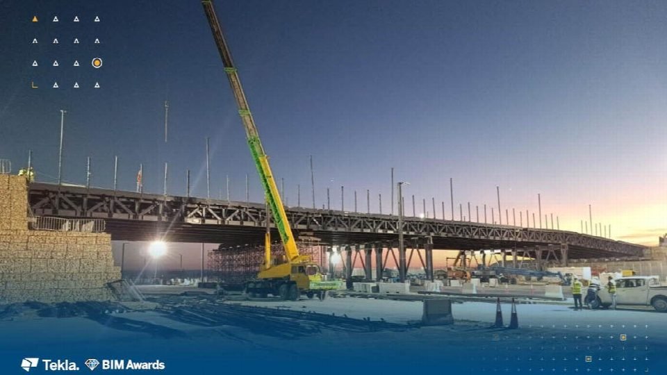 The steel truss bridge erected on its supports at dusk, with a mobile crane standing by.